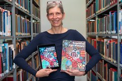 Anja holds a colorful book on Cell Biology in one hand, and an iPad displaying the same e-book in the other.