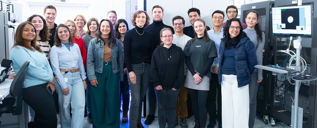 Diverse group of smiling individuals standing in a lab, surrounded by computer servers and monitors.
