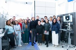 A diverse group of people gathered in a modern laboratory featuring advanced computer systems and technical equipment, including an electron microscope.
